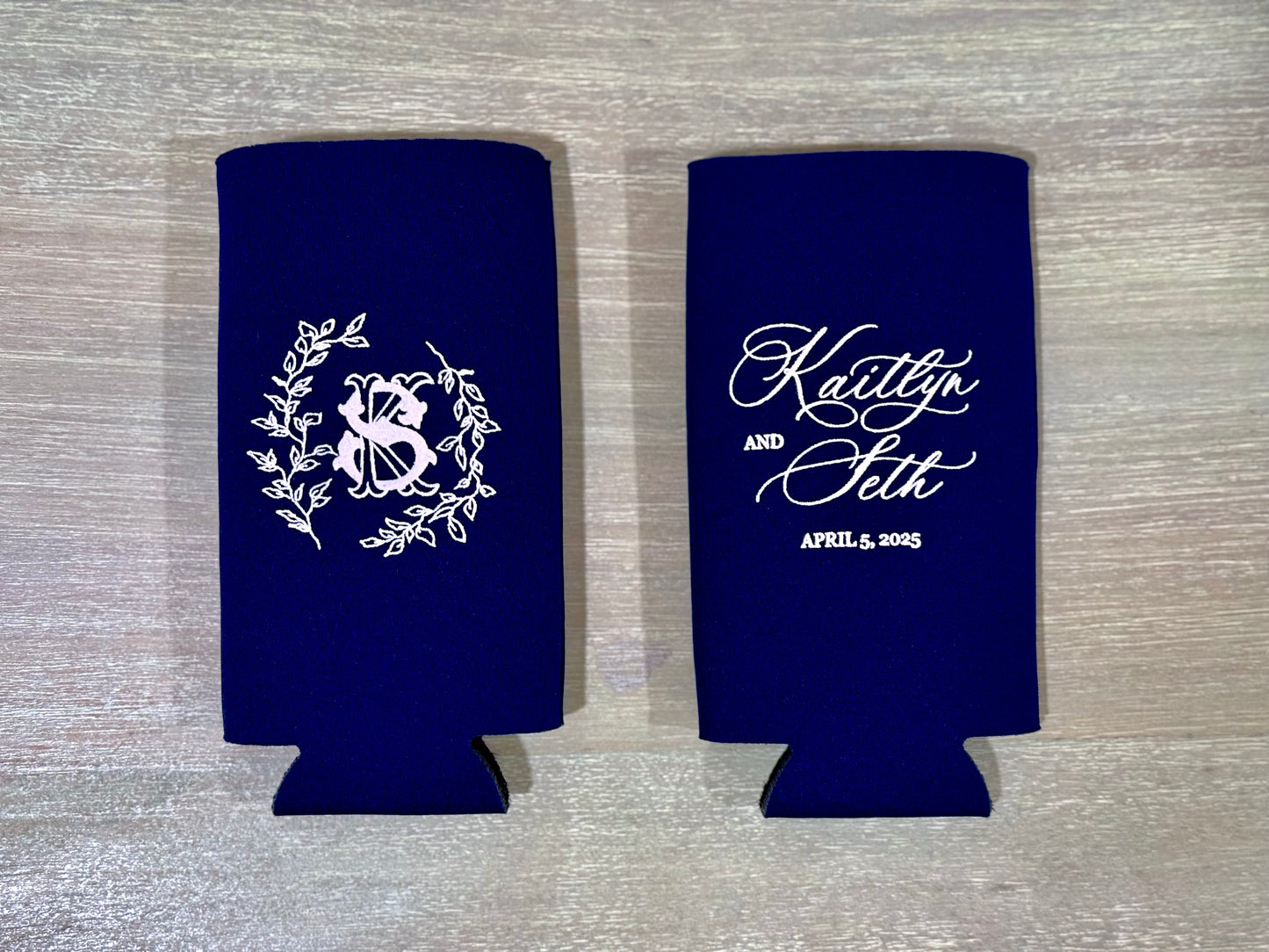 Two navy blue can coolers with white designs on a wooden surface